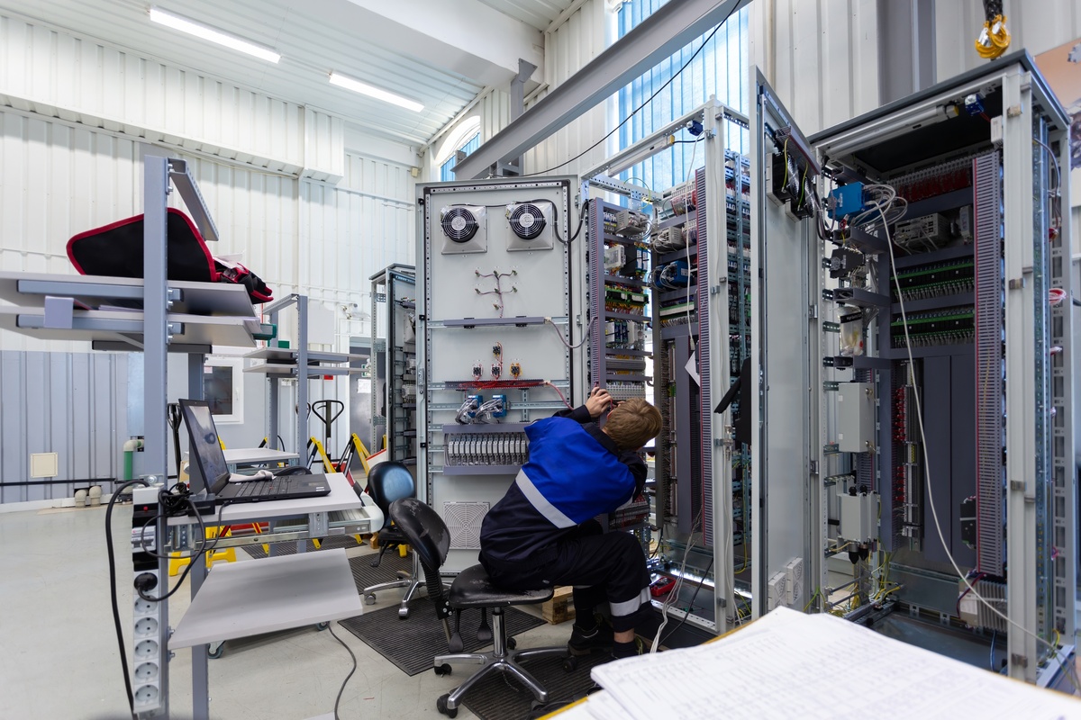 Technician wiring an industrial control panel with terminal blocks, DIN-rail components, PLC hardware, and organized wire duct.