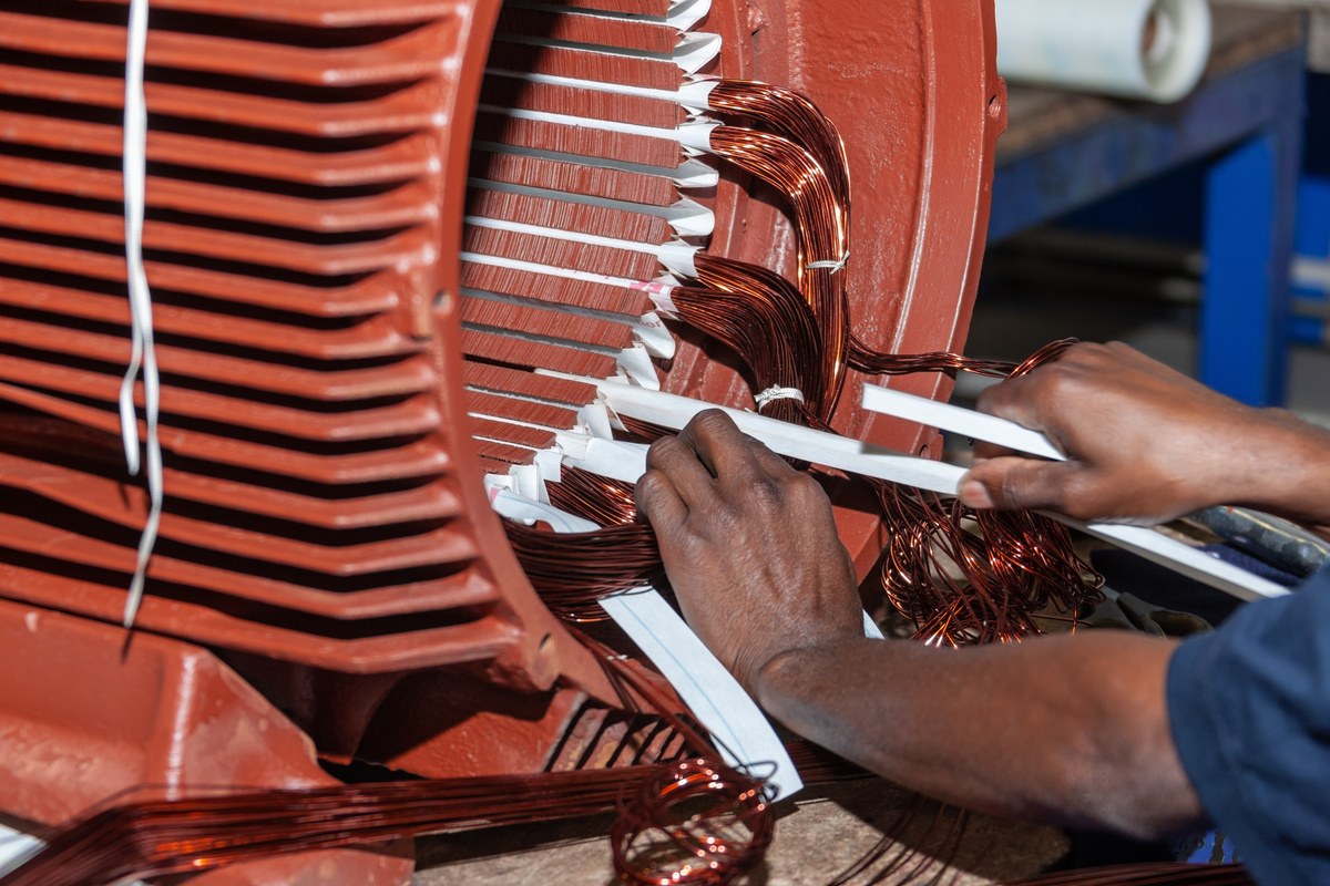 Technician inspecting and rebuilding industrial rotating equipment with an exposed motor stator and measured components.