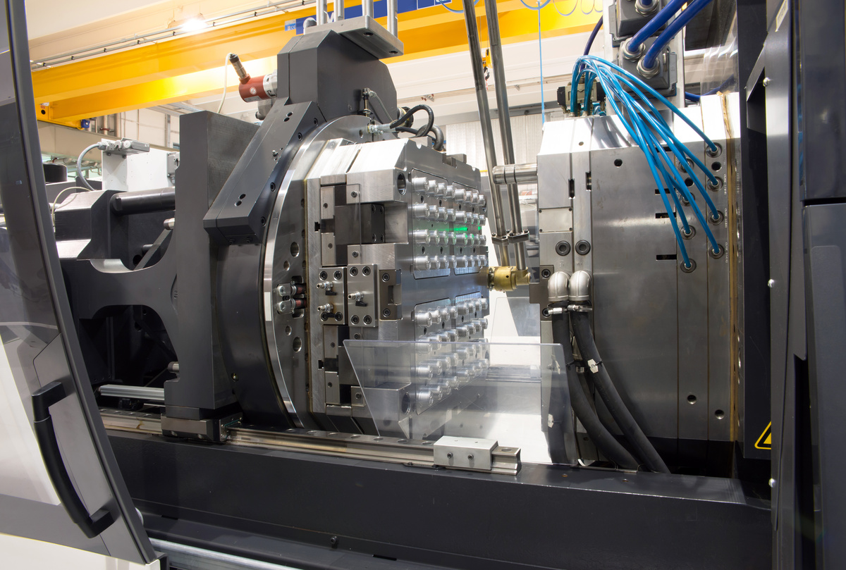 Industrial injection molding machine forming plastic parts, with the mold and clamping unit visible in a plastics manufacturing facility.