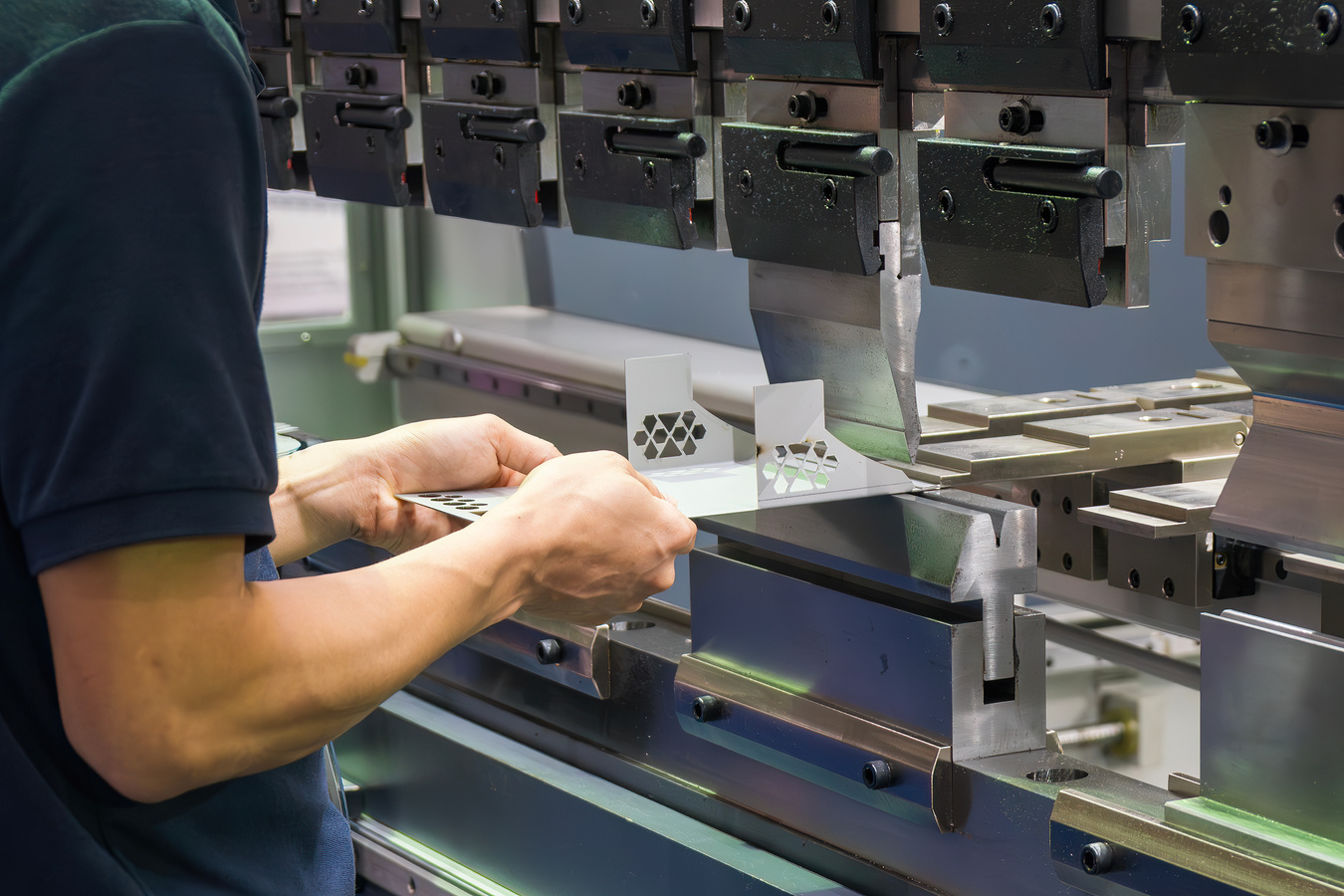 Machine operator positioning a precision sheet metal component in an industrial press brake for controlled bending and metal fabrication.