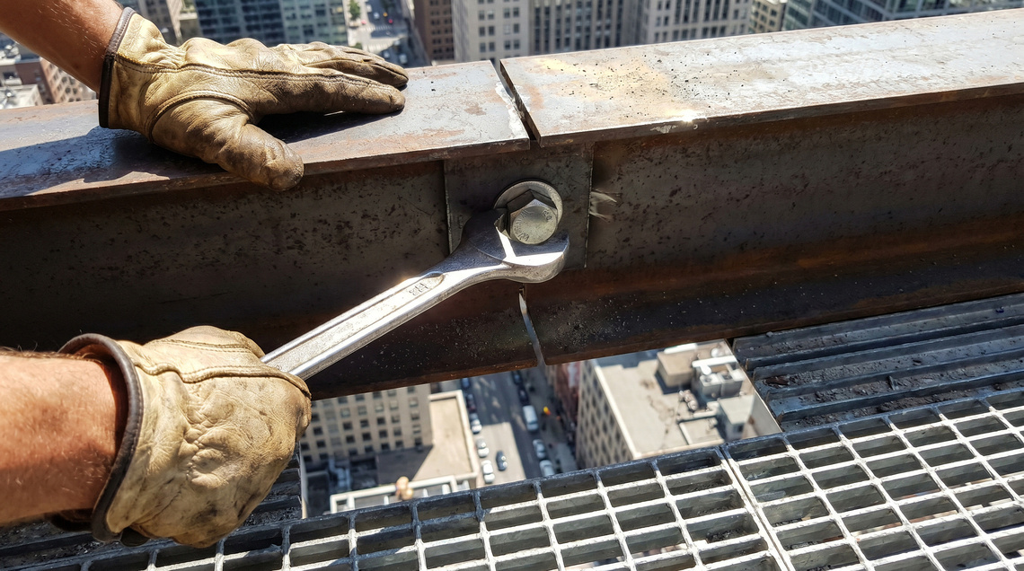 Ironworker tightening a structural bolt with a wrench during steel frame construction.