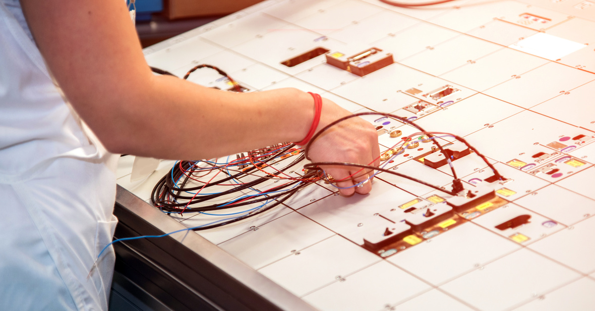 Technician assembling a wire harness on a formboard with routed conductors, branch points, and connectors.